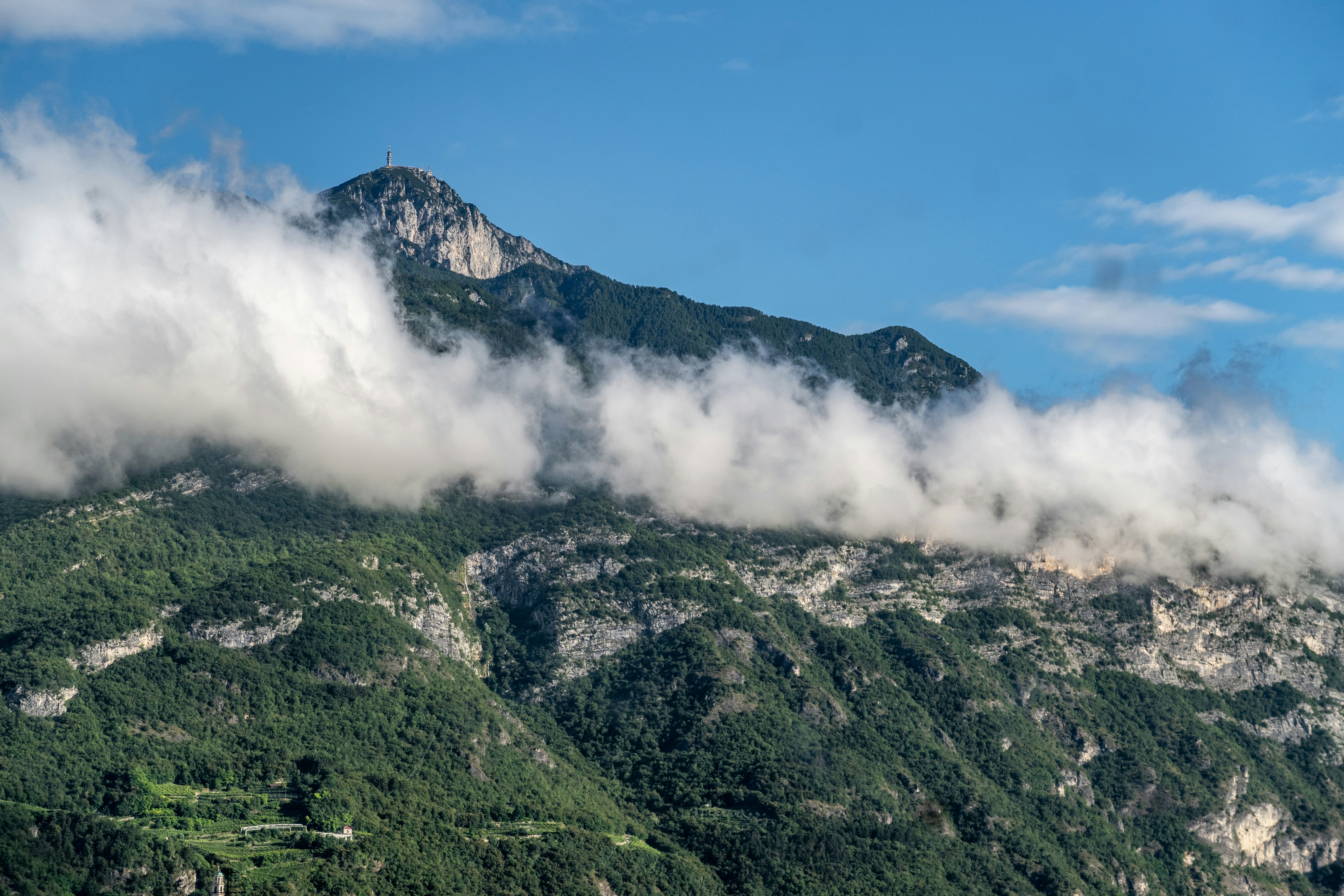 Ein mit Wolken und Bäumen bedeckter Berg unter blauem Himmel
