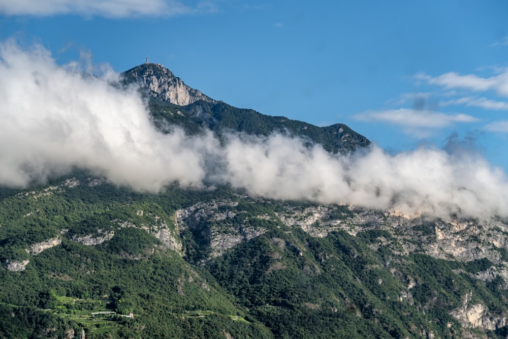 a mountain covered in clouds and trees under a blue sky