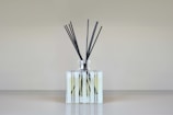 Close-up of a reed diffuser in a clear glass bottle with ivory satin ribbon and minimalist couple name tag.