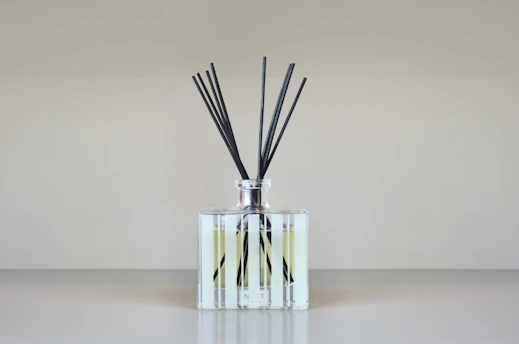 A serene reed diffuser with soft natural light highlighting its elegant glass bottle and wooden reeds on a minimalist white surface.