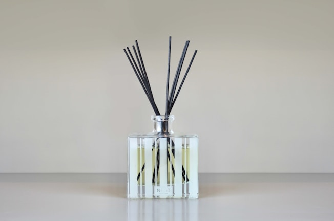Close-up of a reed diffuser in a clear glass bottle with ivory satin ribbon and minimalist couple name tag.