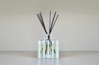 A reed diffuser with slender reeds in a sleek glass bottle, placed on a minimalist shelf.