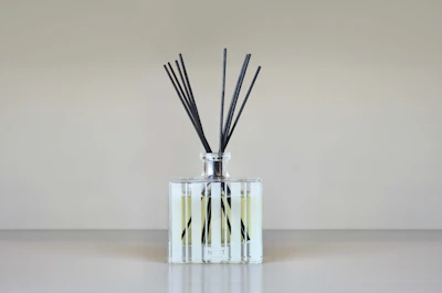 A reed diffuser with slender reeds in a sleek glass bottle, placed on a minimalist shelf.