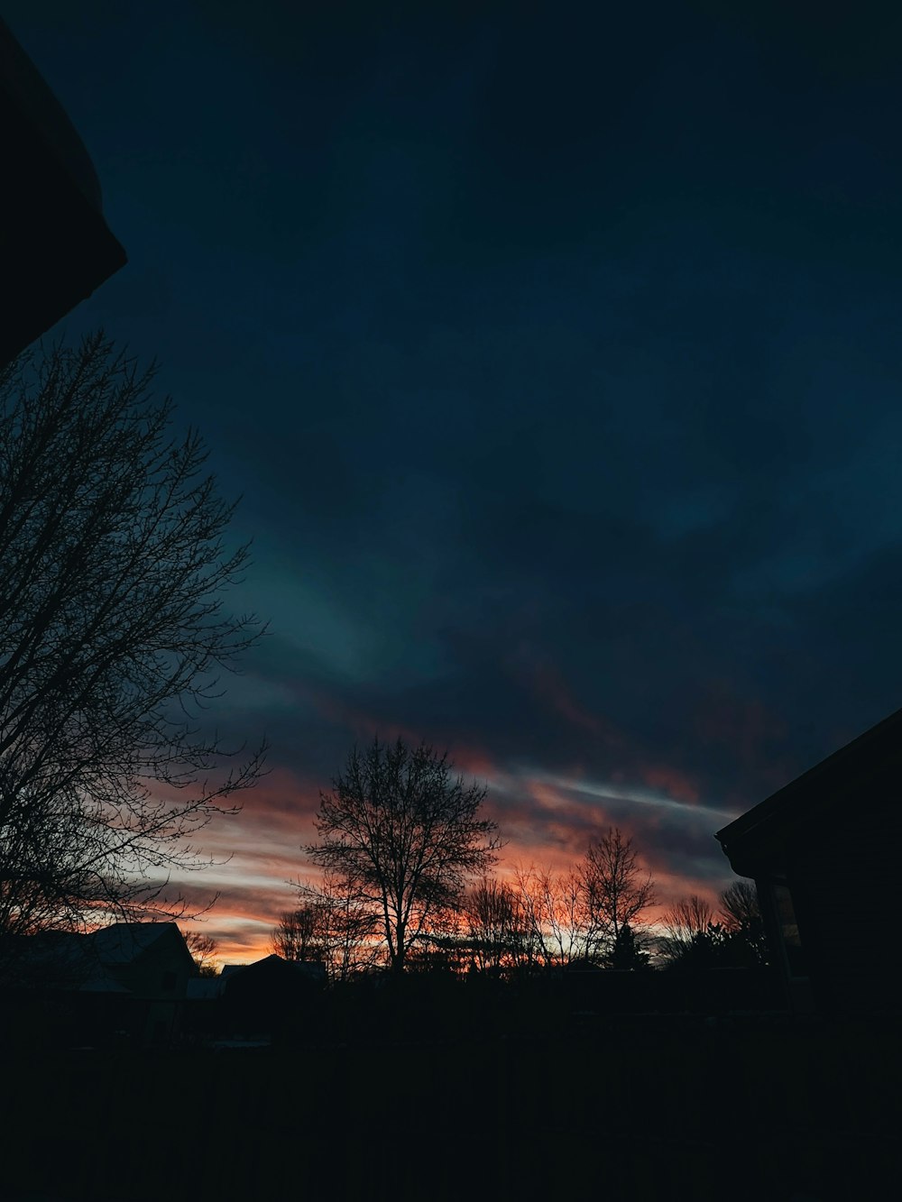 a dark sky with clouds and trees in the foreground