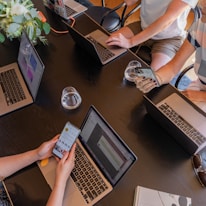 a group of people sitting around a table with laptops
