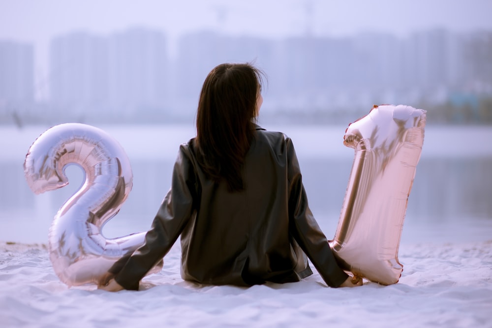 a woman sitting in the sand with two balloons