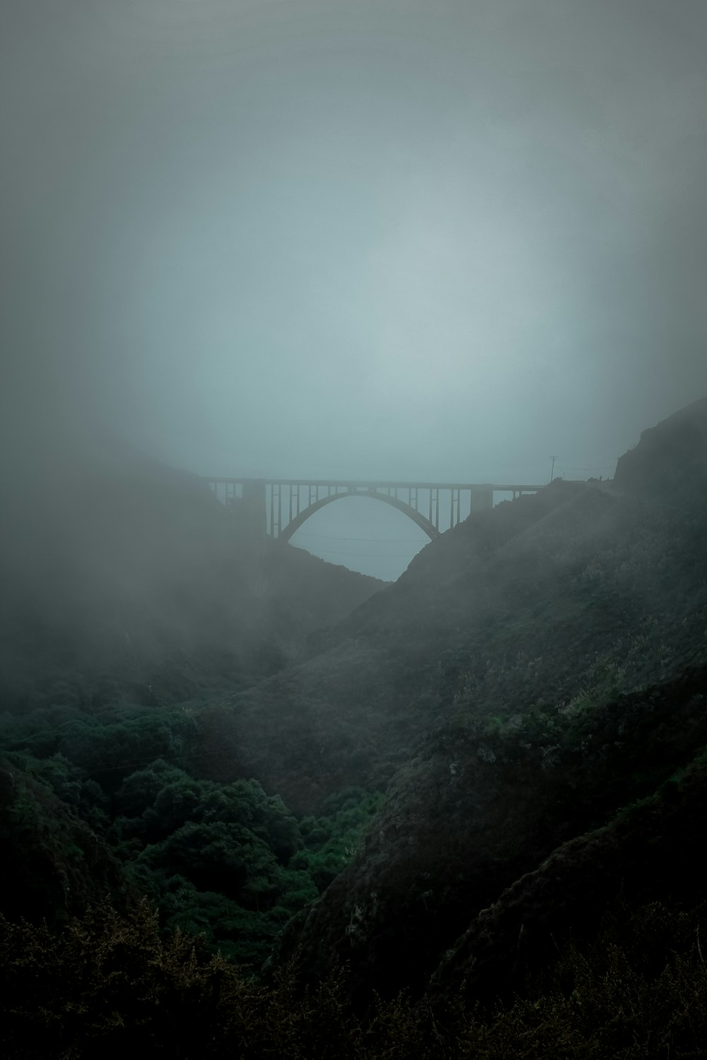 a foggy landscape with a bridge in the distance