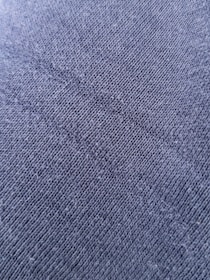A close-up view of a textured fabric surface with tightly woven fibers forming a diagonal pattern. The material appears to be a dark shade of blue or charcoal grey, with a slightly rough and grainy texture.
