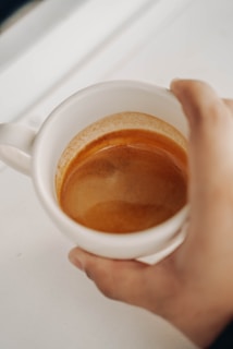 A hand holding a perfectly pulled espresso shot above a Bodhi Beans branded saucer, with a blurred cozy kitchen background