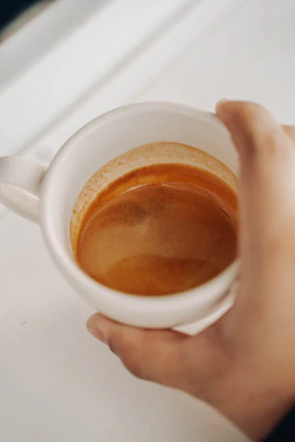 A steaming espresso shot pouring into a classic white ceramic cup with crema visible on top.