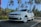A white car with the license plate 'KL 58 U 2314' is parked on a road lined with tall palm trees under a clear blue sky.