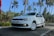 A white car with the license plate 'KL 58 U 2314' is parked on a road lined with tall palm trees under a clear blue sky.