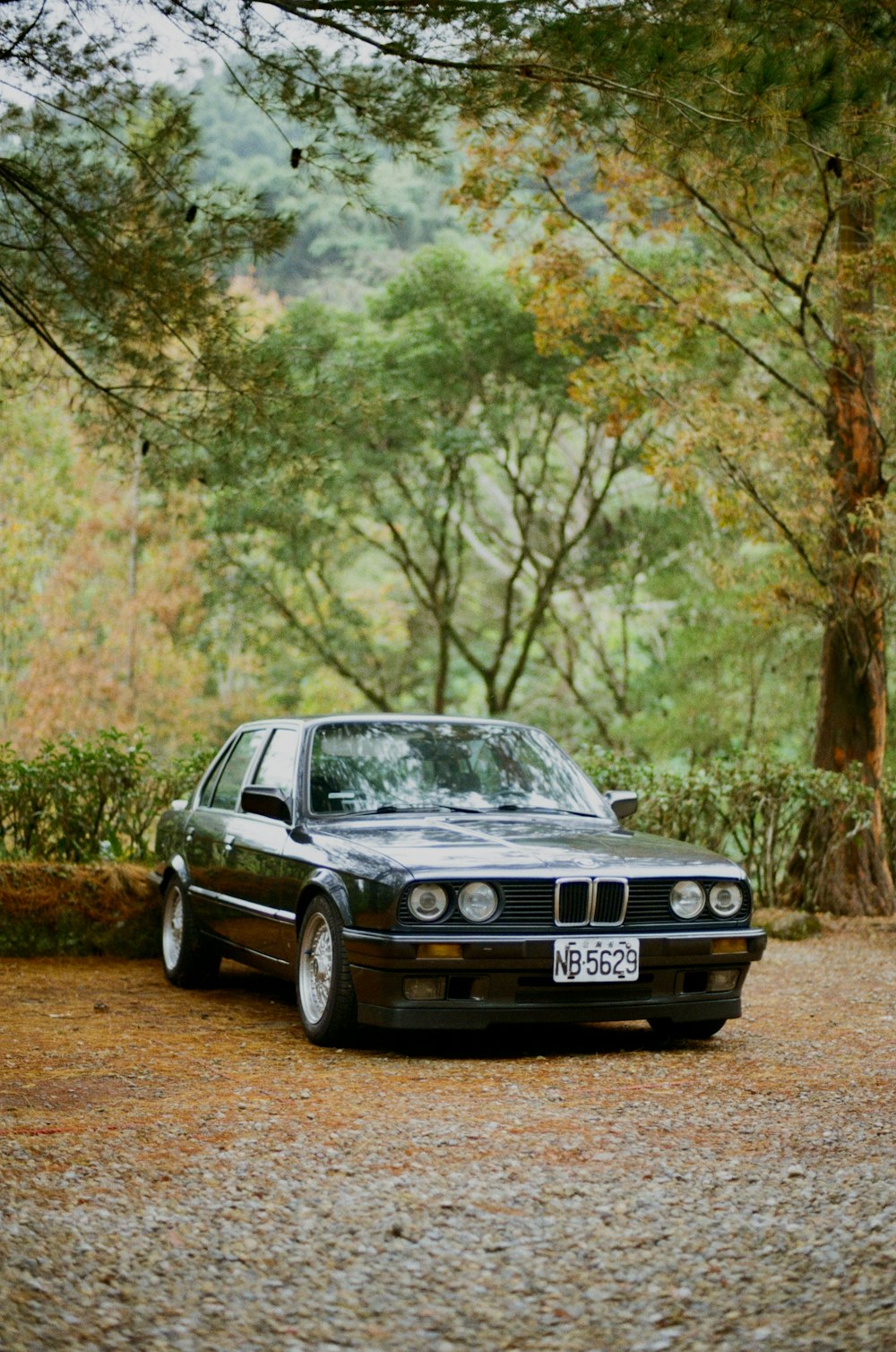 a black car parked on a gravel road next to trees