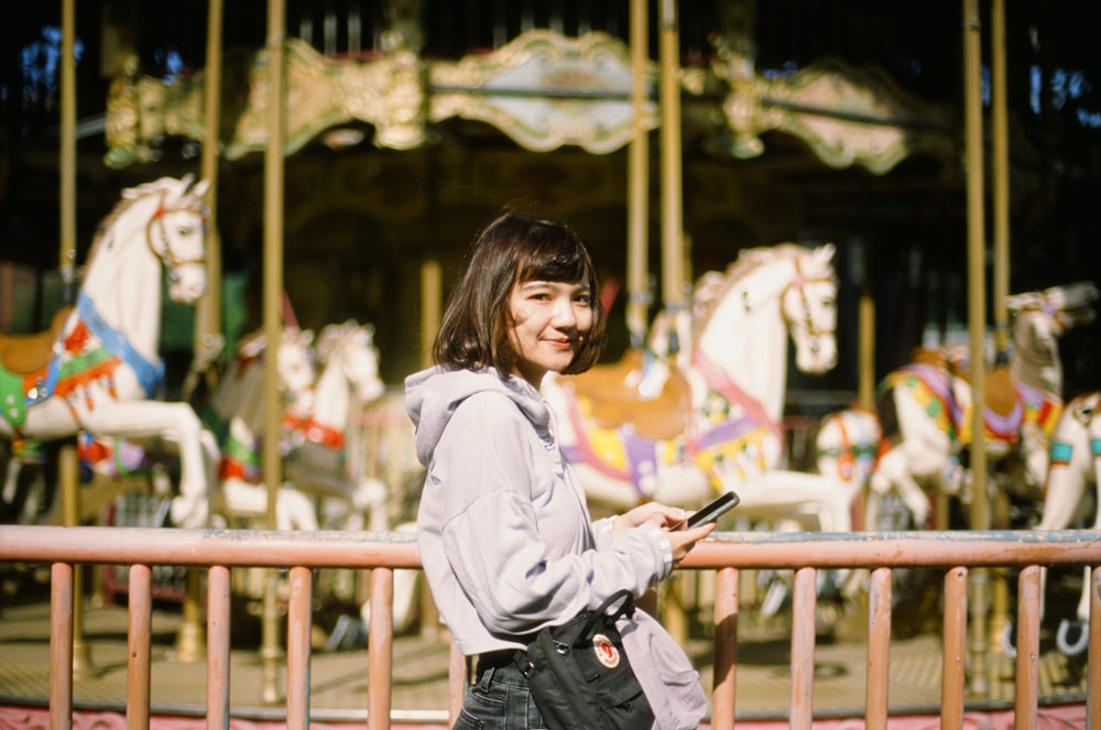 a woman standing in front of a carousel with a cell phone