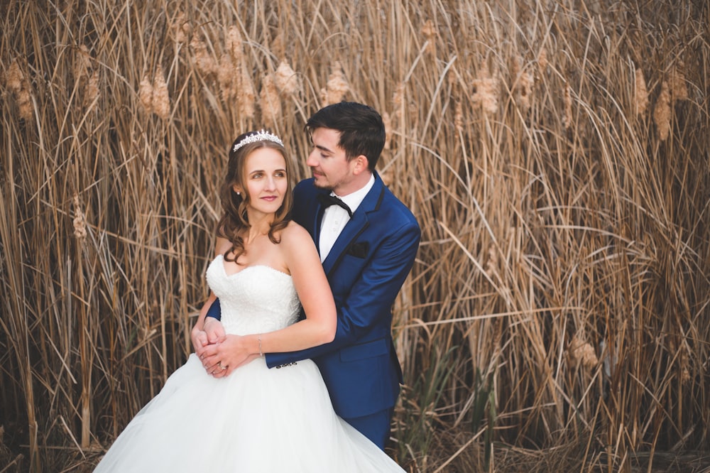 a bride and groom standing in front of tall grass