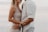 A couple standing closely together, partially visible, showcasing intimate body language. The woman wears a light-colored dress, and the man is in a white shirt. There is a soft and serene background, likely a beach setting.