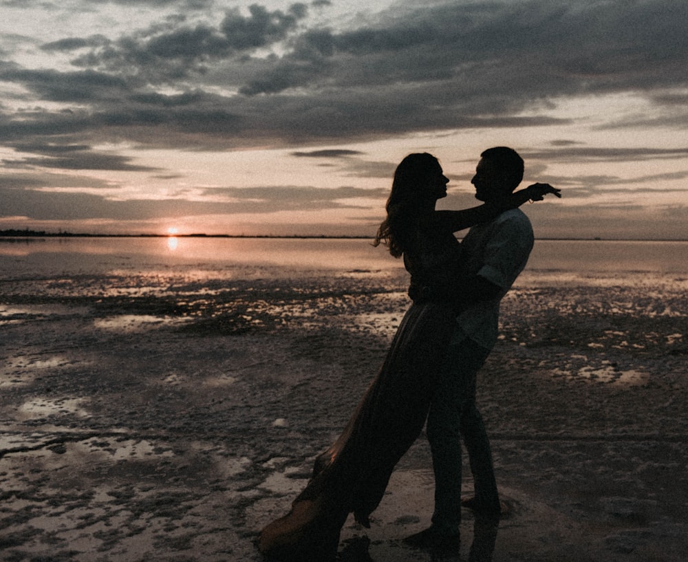 a man and a woman standing on a beach at sunset