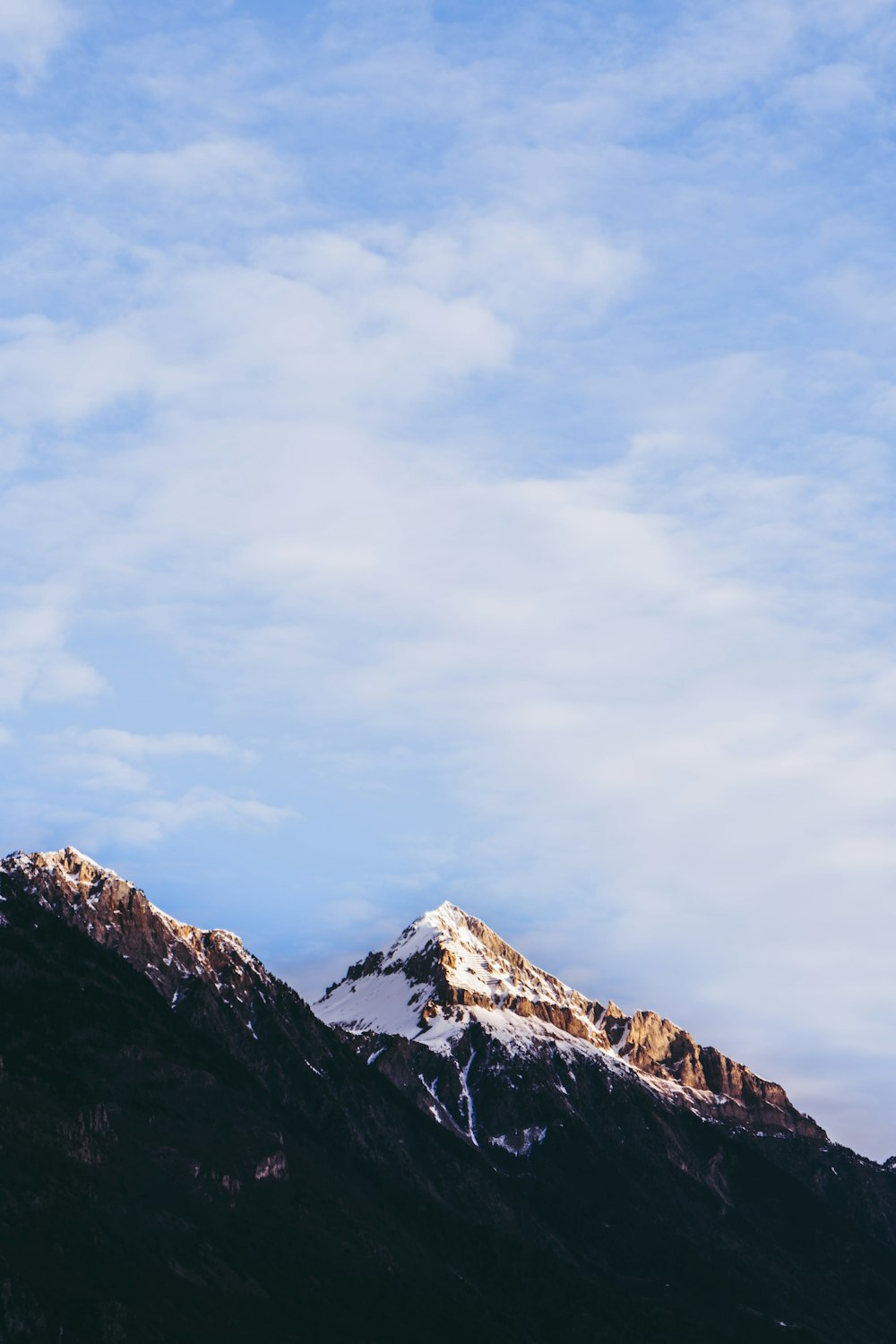 a snow covered mountain under a cloudy blue sky