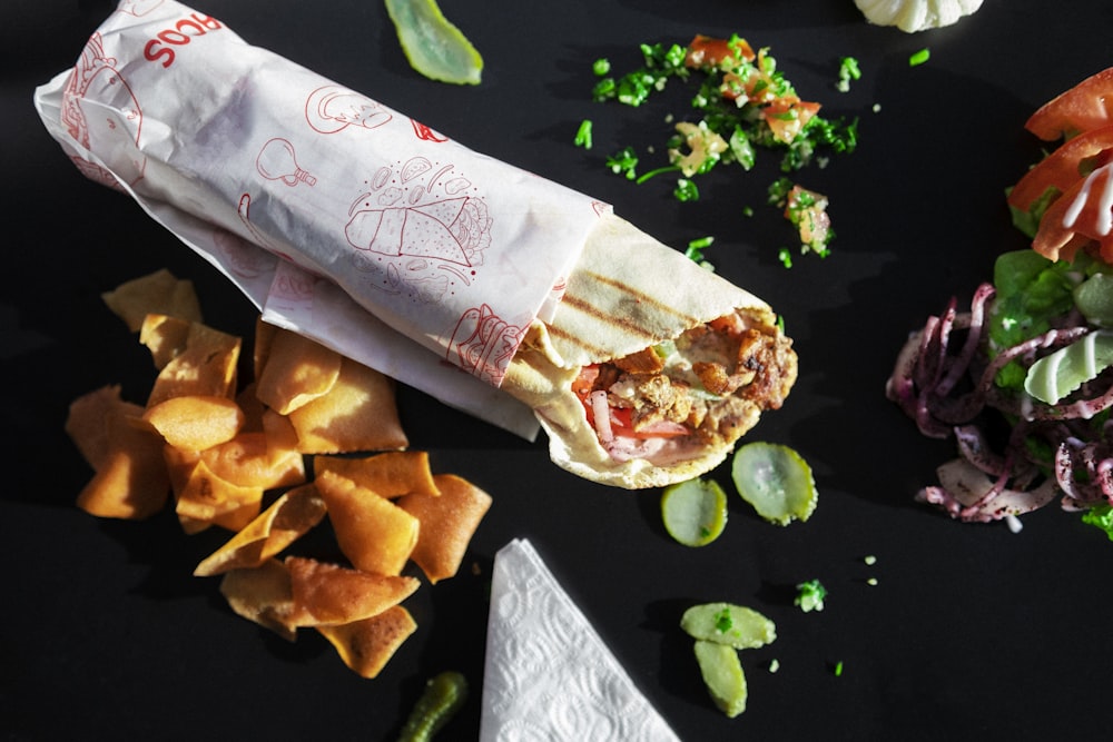 a sandwich with a wrapper and chips on a table