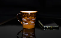 a coffee cup sitting on top of a table next to a cell phone