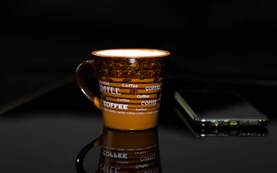 a coffee cup sitting on top of a table next to a cell phone