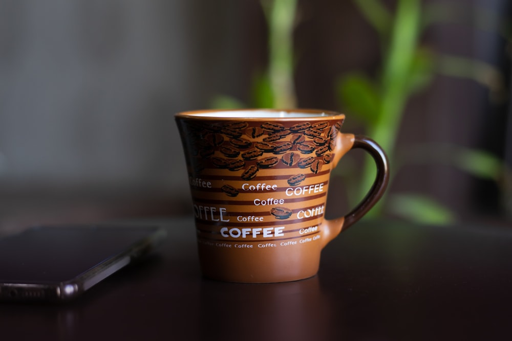 a coffee cup sitting on a table next to a cell phone