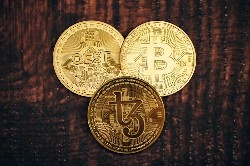 three gold bitcoins sitting on top of a wooden table