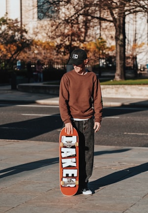 a young man holding a skateboard on a sidewalk