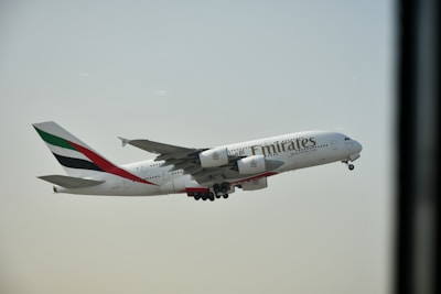 An Airbus A380 airplane bearing the Emirates airline branding is in mid-flight against a clear sky. The aircraft's engines and landing gear are visible.