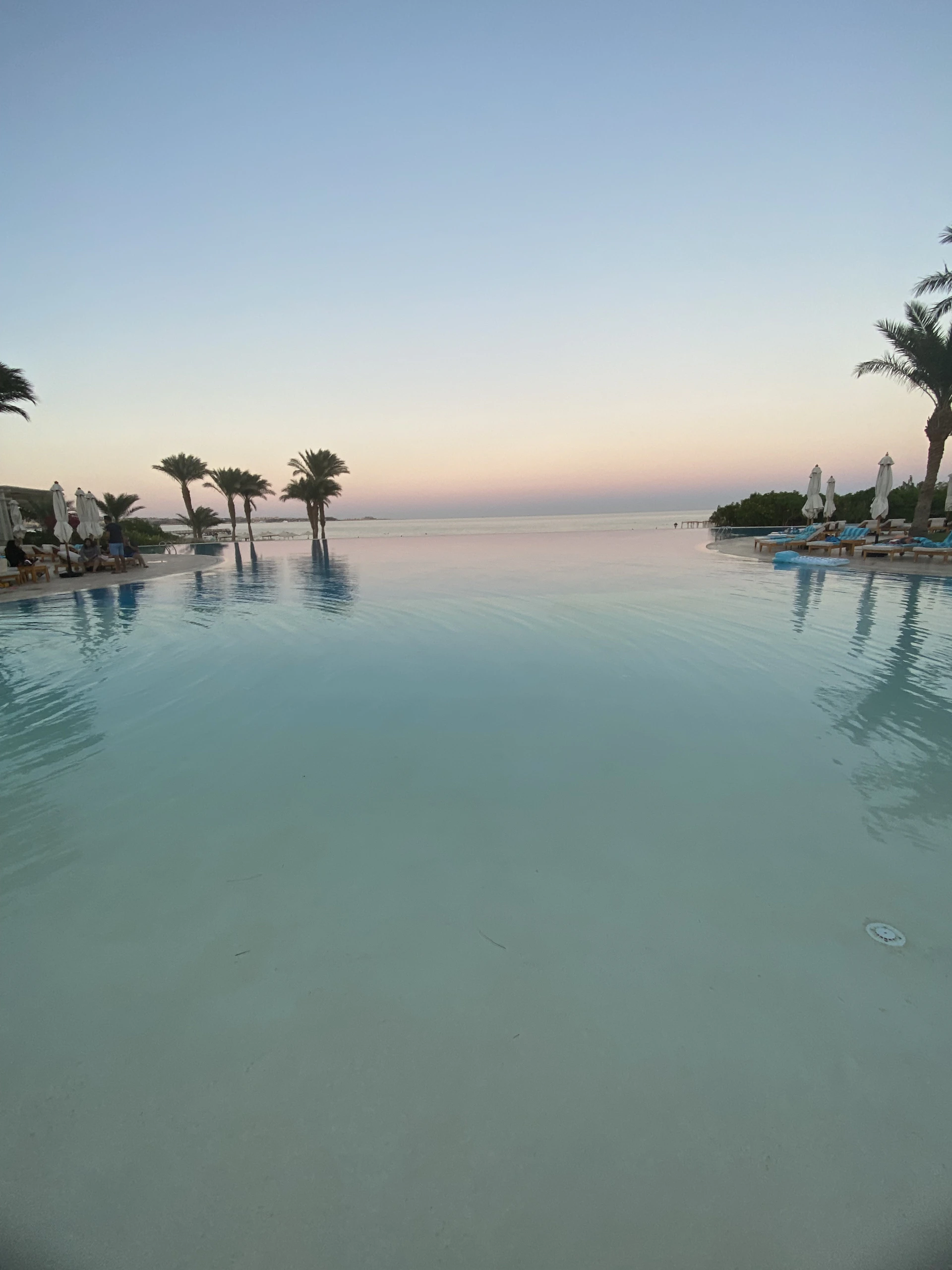 An inviting infinity pool at dusk with soft lighting, surrounded by elegant loungers and tropical plants.
