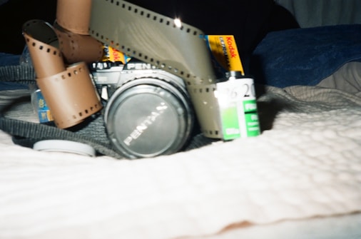 An analog camera with a coiled film strip on top, accompanied by Kodak and Fujifilm film canisters. The camera rests on a textured surface, creating a nostalgic, vintage feel.