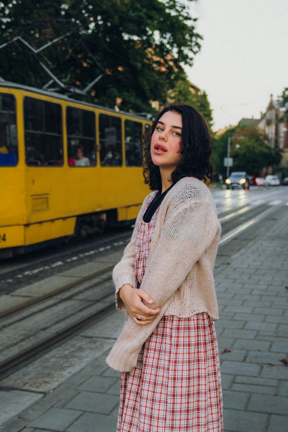 a woman standing on a sidewalk next to a yellow train