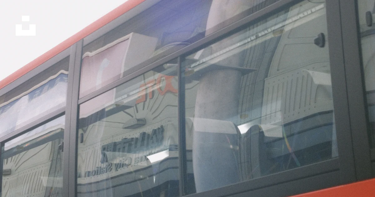 A red double decker bus with a reflection of a person in the window ...