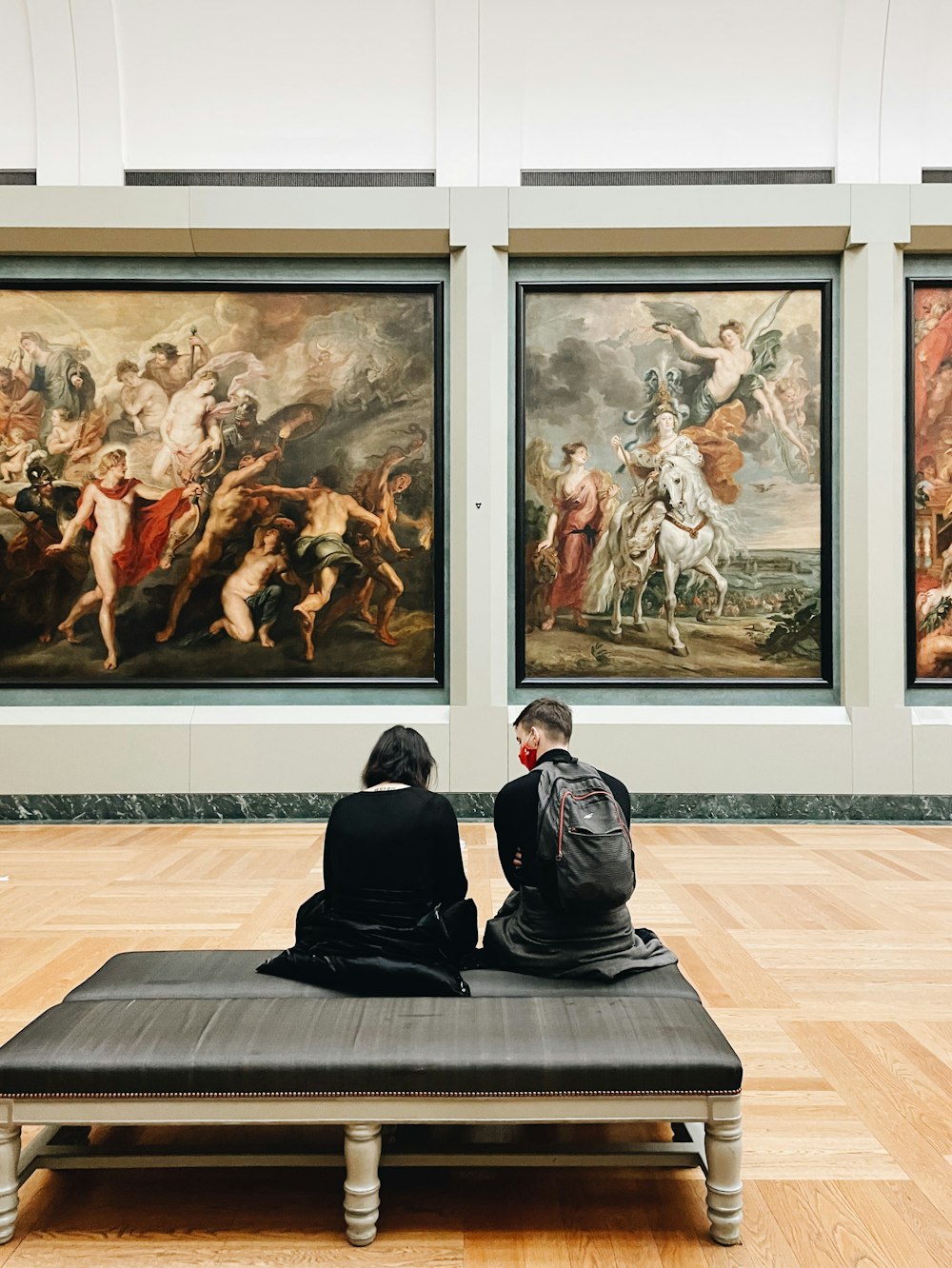 two people sitting on a bench in front of paintings