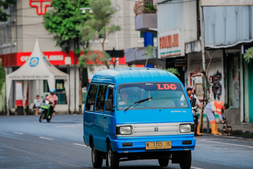 a blue van driving down a street next to tall buildings
