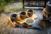 a wooden tray topped with three cups filled with green tea