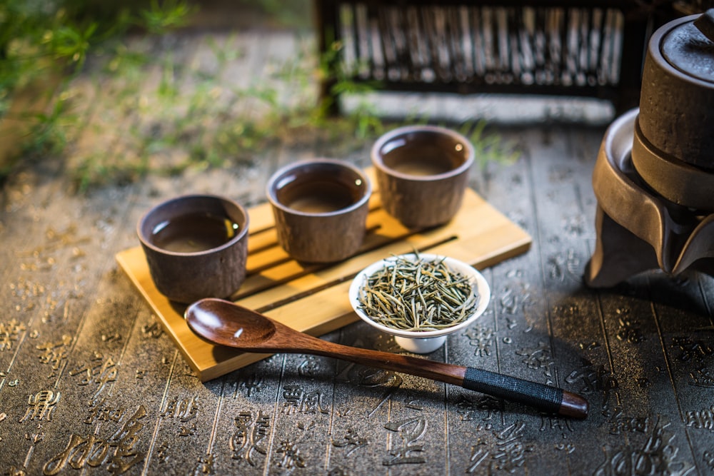 a wooden tray topped with three cups filled with green tea
