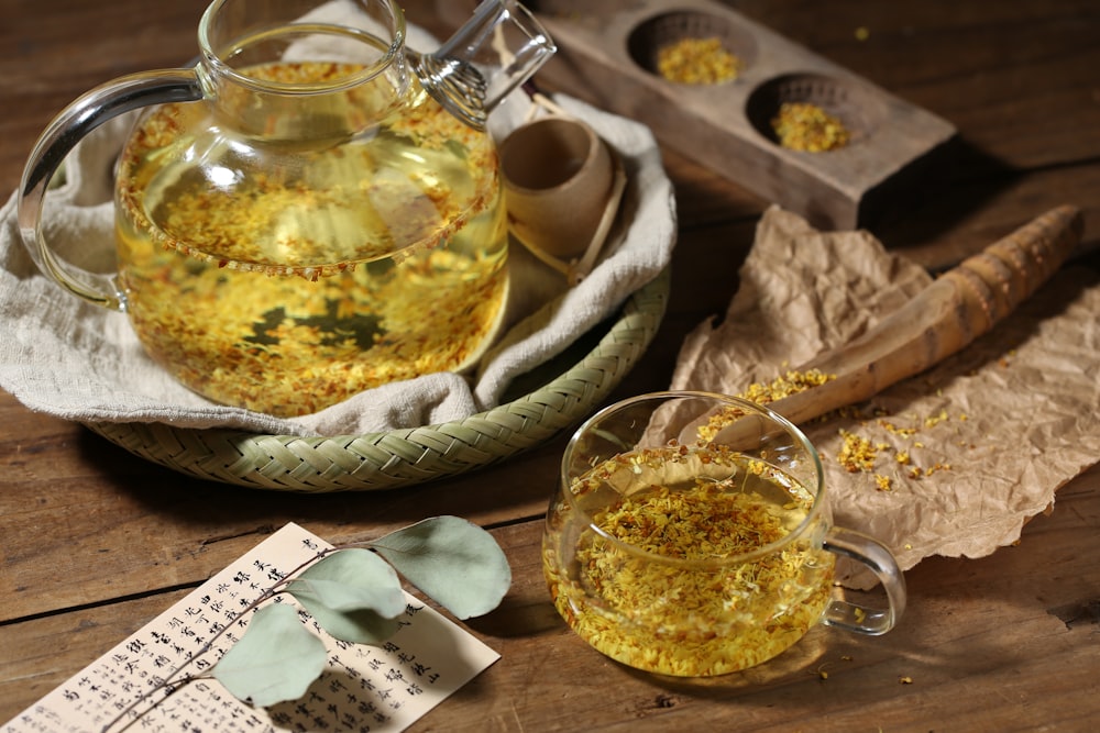 a glass teapot filled with yellow liquid next to a cup of tea