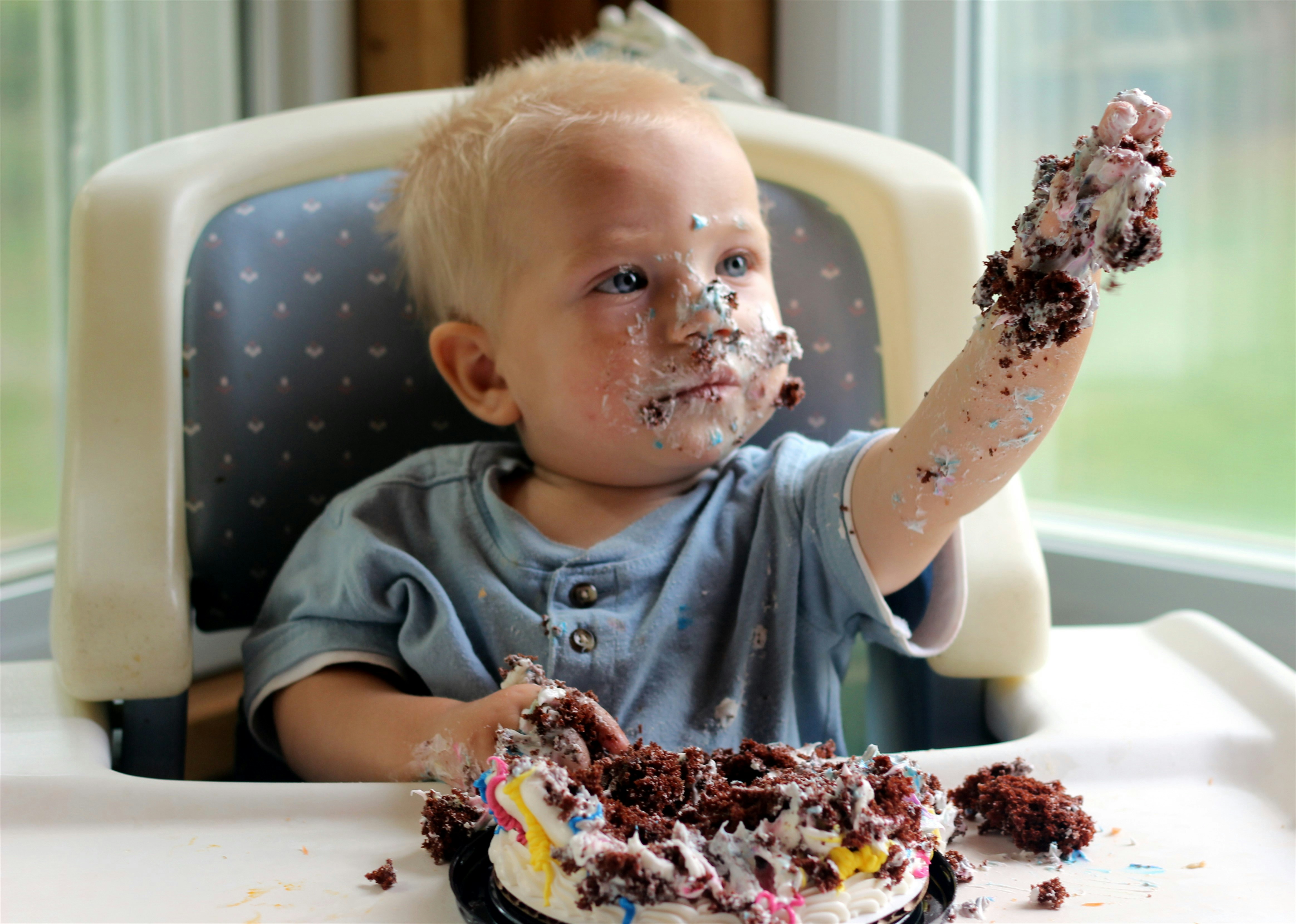 Messy toddler covered in cake with a birthday cake.