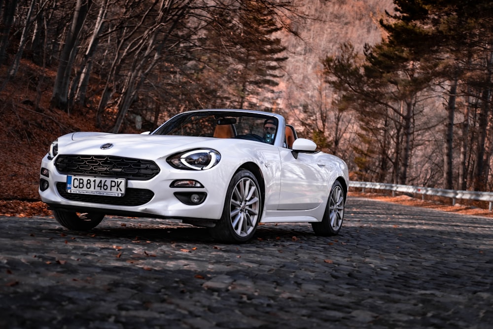 a white car driving down a road next to a forest