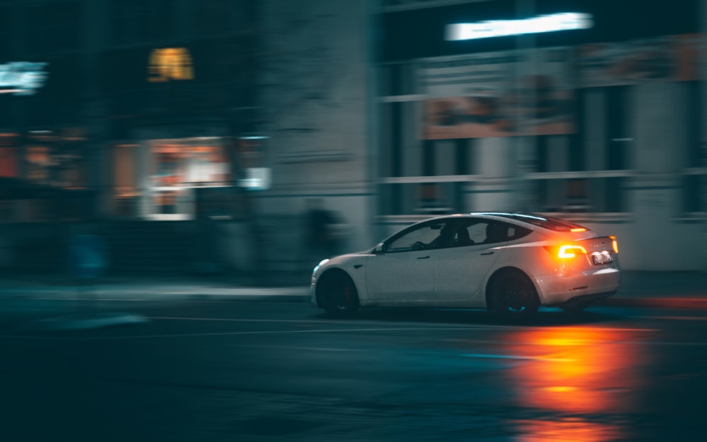 a white car driving down a street at night