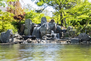 a pond with a waterfall surrounded by rocks and trees