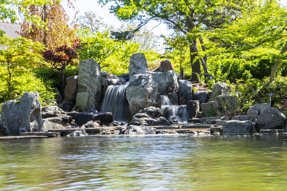 a pond with a waterfall surrounded by rocks and trees