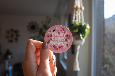 a person holding a pink sticker that says enjoy every moment