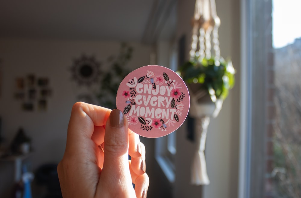a person holding a pink sticker that says enjoy every moment
