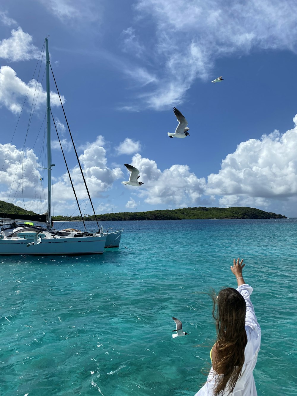 a woman standing in the water looking at a sailboat