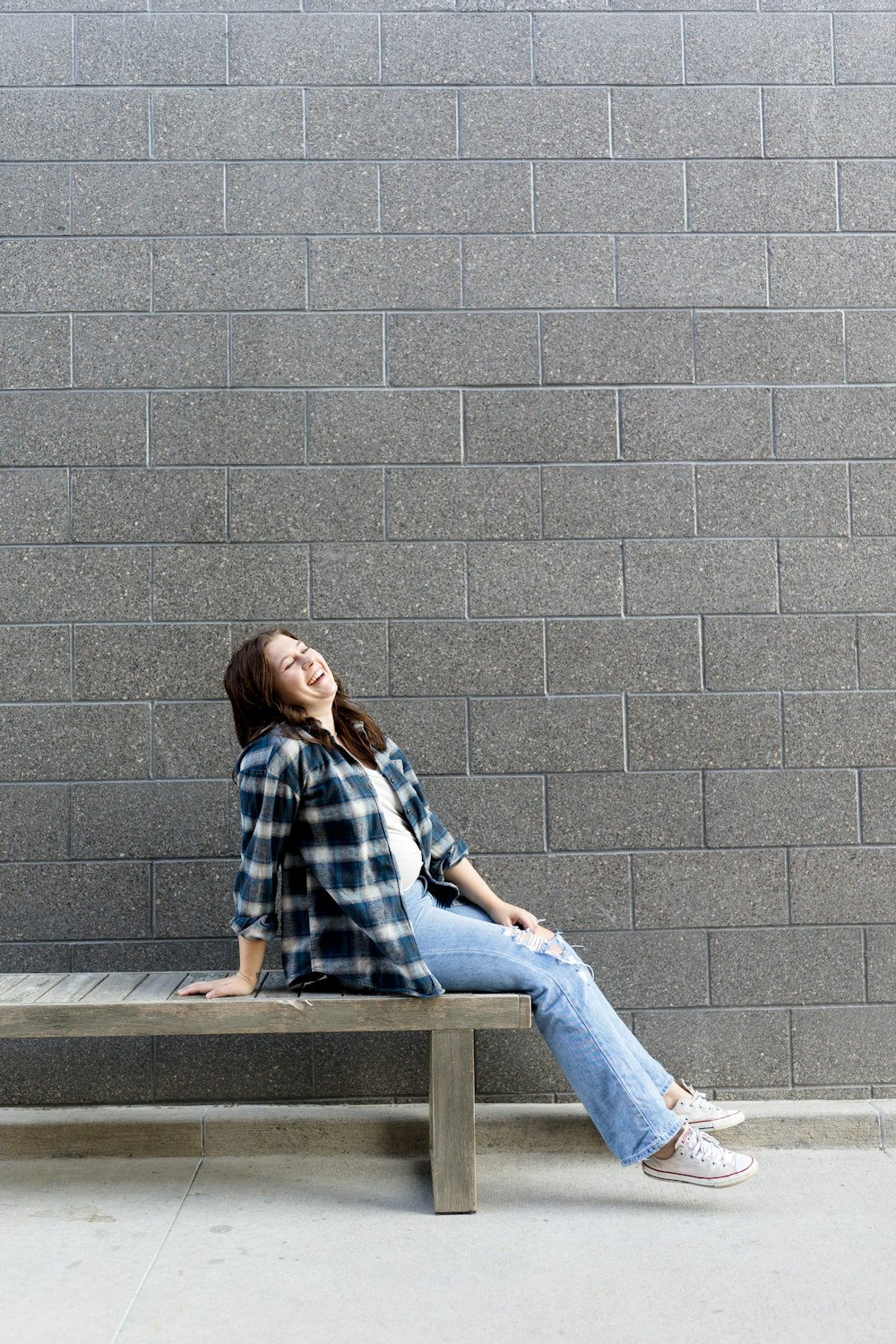 a woman sitting on a bench in front of a brick wall