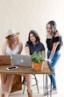 three women sitting at a table looking at a laptop
