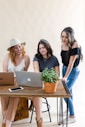 three women sitting at a table looking at a laptop