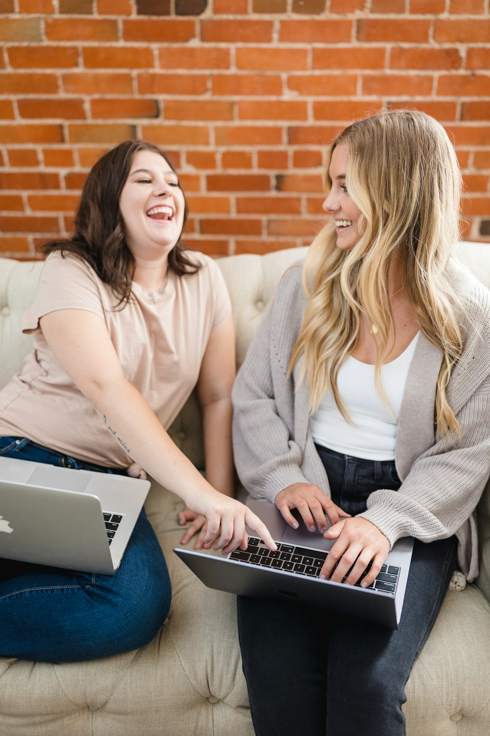 two women sitting on a couch with laptops